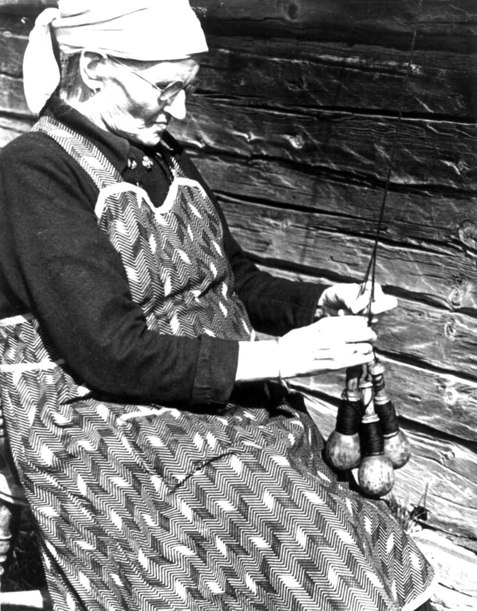 Slingring. Anne Østby fletter garn ved hjelp av garnsneller. Røros, Sør-Trøndelag 1939.