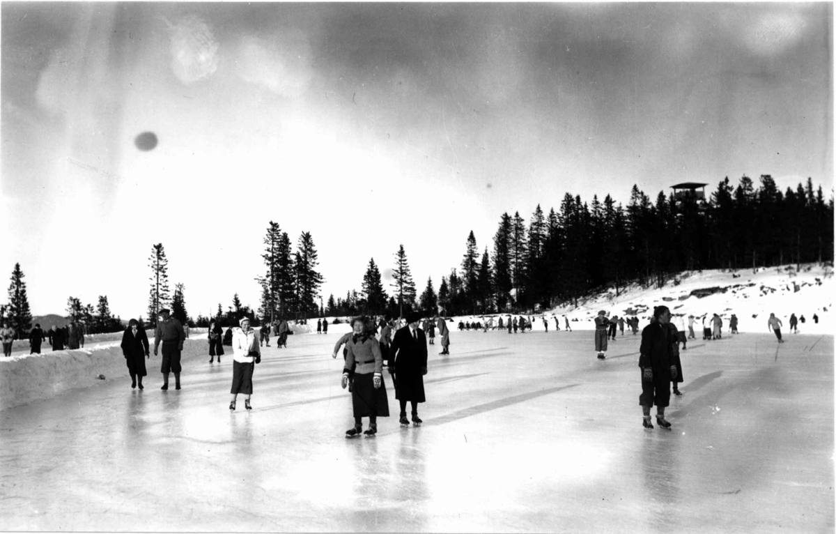 Tryvann skøytebane, Oslo. 1935. Skøyteløpere i sving på isen. Toppen av Tryvannstårnet ses i bakgrunnen.