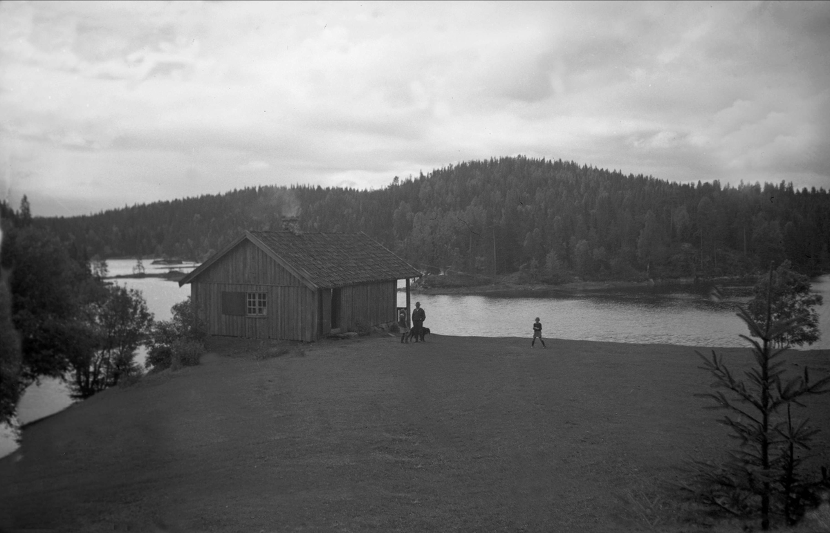 En mann og to barn står ved en hytte som ligger ved Børtervann, Enebakk. Fotografert 1936.