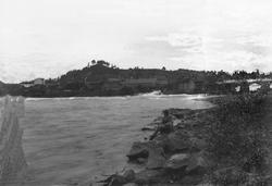 En mann sitter på en sten og skuer ut over elven ved Hønefos