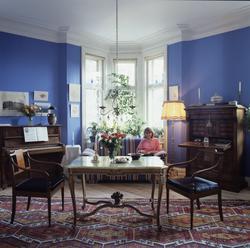 En stue med skatoll, bord og stoler, sofa,et piano, lamper o