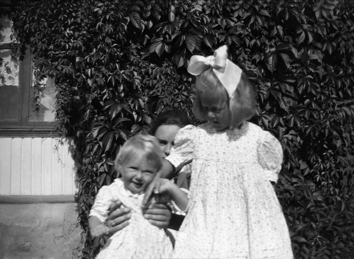 En kvinne og to barn poserer i en hage. Robsahm og Lund.
