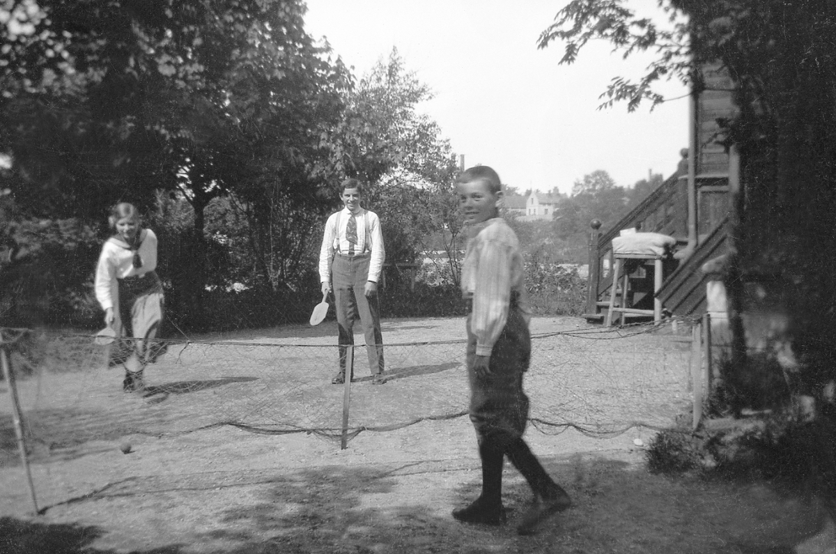 Sofie, Fritjof og Bjarne Arentz spiller tennis med trefjeler foran hjemmet Elverhøy i Trondheim. I bakgrunnen en hjemmelaget " hoppebukk".