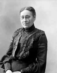 Portrett, kvinne i svart kjole, med briller.