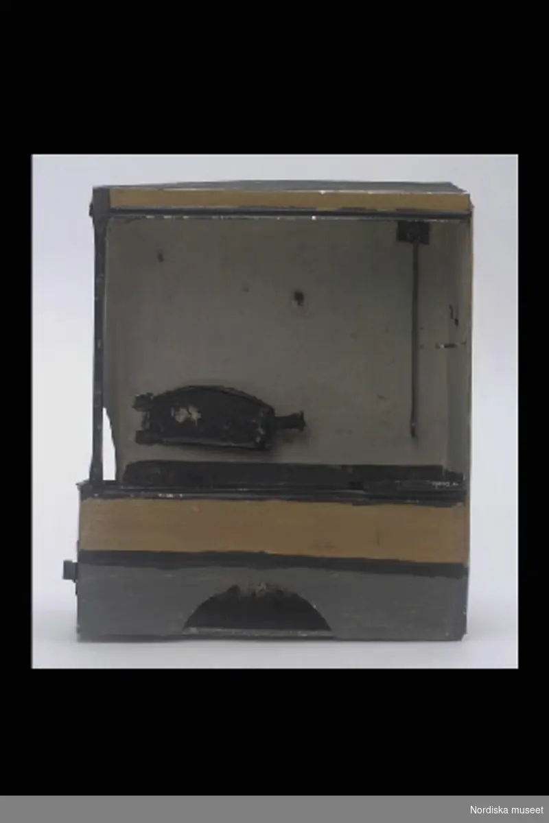 Inventering Sesam 1996-1999:
a) Spis L 20 cm, B 9 cm, H 24 cm
b) Långpanna L 8,8 cm, B 5,3 (med snås)
a) Öppen, rektangulär köksspis av plåt med spiskåpa. Målad i grått, gult och svart. I bakväggen bakugn och spjäll, till vänster på härden en kokgruva. Nertill halvcirkelformad öppning fram och liten lucka på vänster kortsida.
b) Långpanna av svart plåt, rektangulär, låg uppvikt kant, handtag på kortändarna, snås i ena hörnet. 
Se bilaga till dockorna i samma gåva.
Leif Wallin nov 1997