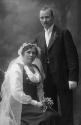 Gruppebilde, bryllupspar. Han i dress, bruden i folkedrakt f