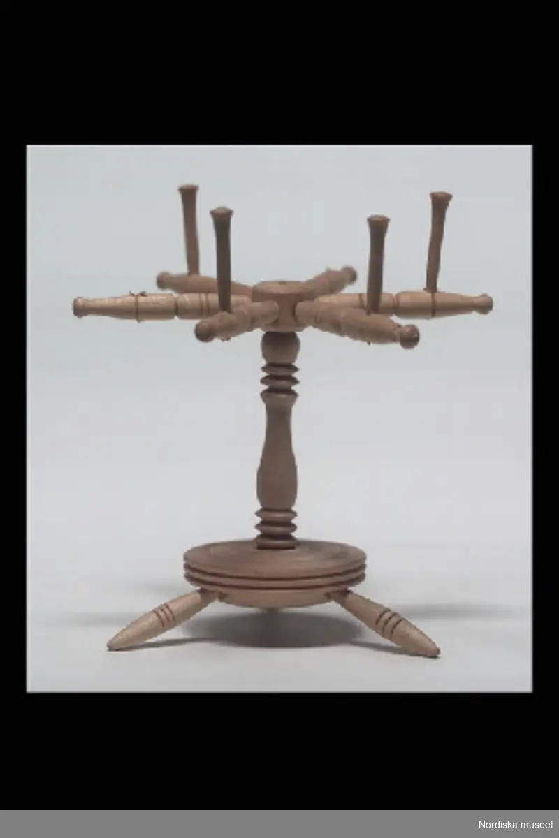 Inventering Sesam 1996-1999:
H 9    B 9  (cm)
Nystvinda, leksak, av obehandlat lövträ, rund svarvad bottenplatta med tre utställda ben, horisontellt placerad vinda med sex armar.
Birgitta Martinius 1997