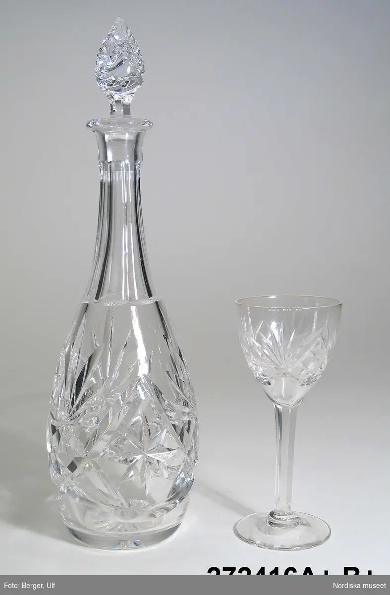 Huvudliggaren:
"Karaffin med 6 glas; trol. halvkristall; slipad dekor av rutmönster coh 'kastar'; kafaffinen ovalt pumpformad, rak slipad hals; propp mönsterslipad. a/ H med propp 26,5 cm, b/ H 12,3 cm, Diam mynning 5,4 cm.
Enl. sälj. Ink. på Gbg-utställn. 1923 av fadern.
I. 21/2 1968 Fröken Gunborg Rundqvist, Stockholm, 100:-."