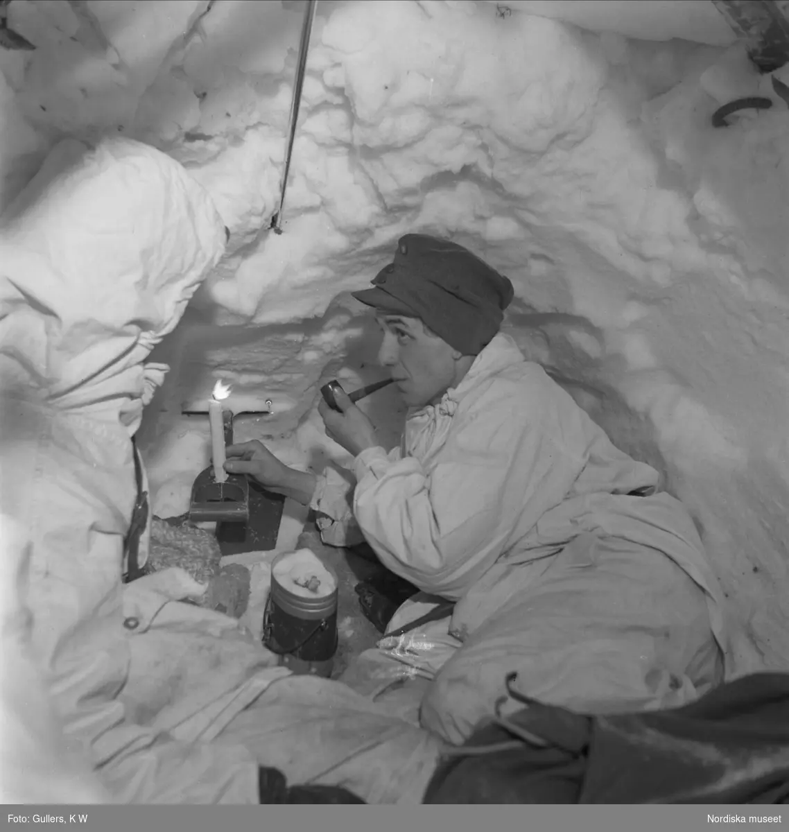 Soldat i snövärn röker pipa vid ett tänt stearinljus