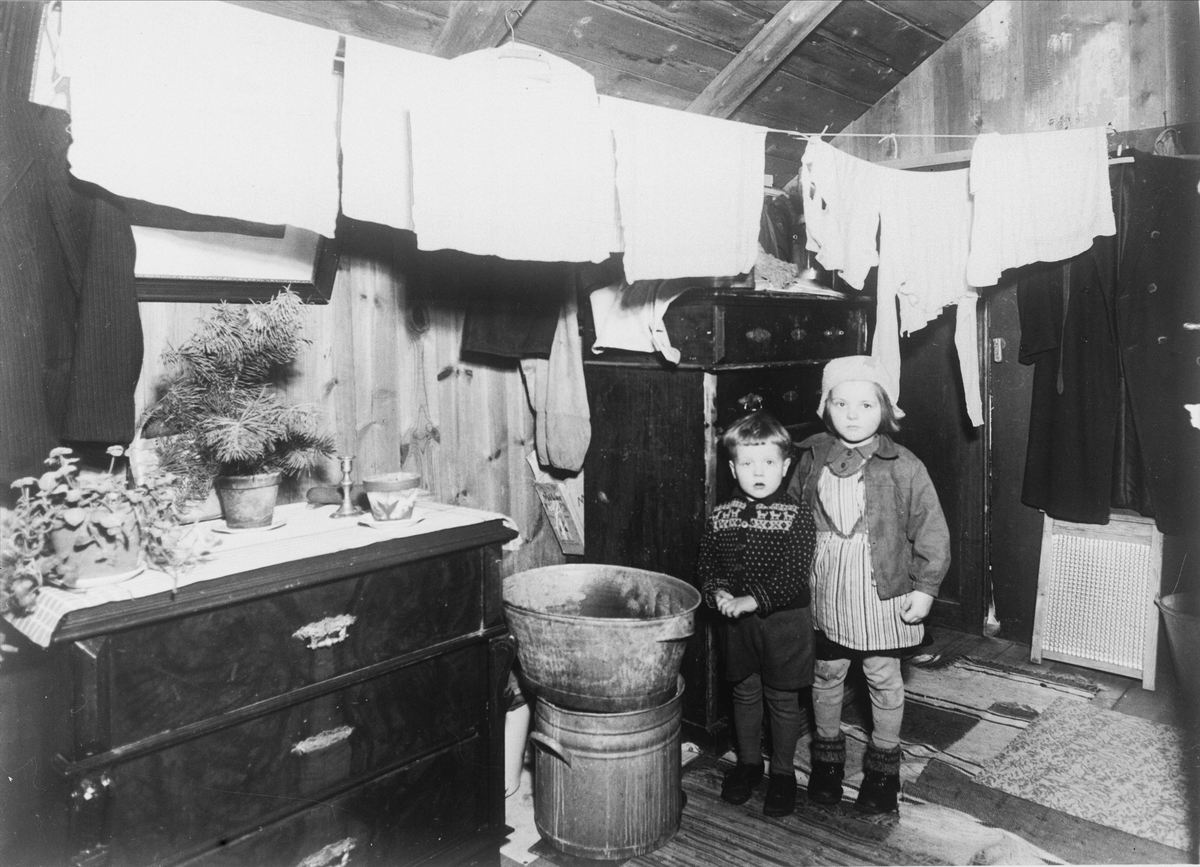 Två barn i trångbott hem. Tvätt hänger på linor under taket.