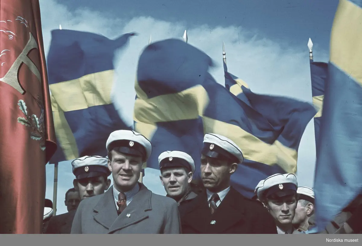Män med studentmössor. Svenska flaggor. Första maj.