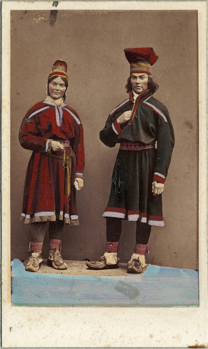 Dräktdockor föreställande n kvinna och en man i samiska dräkter. Handkolorerat foto.