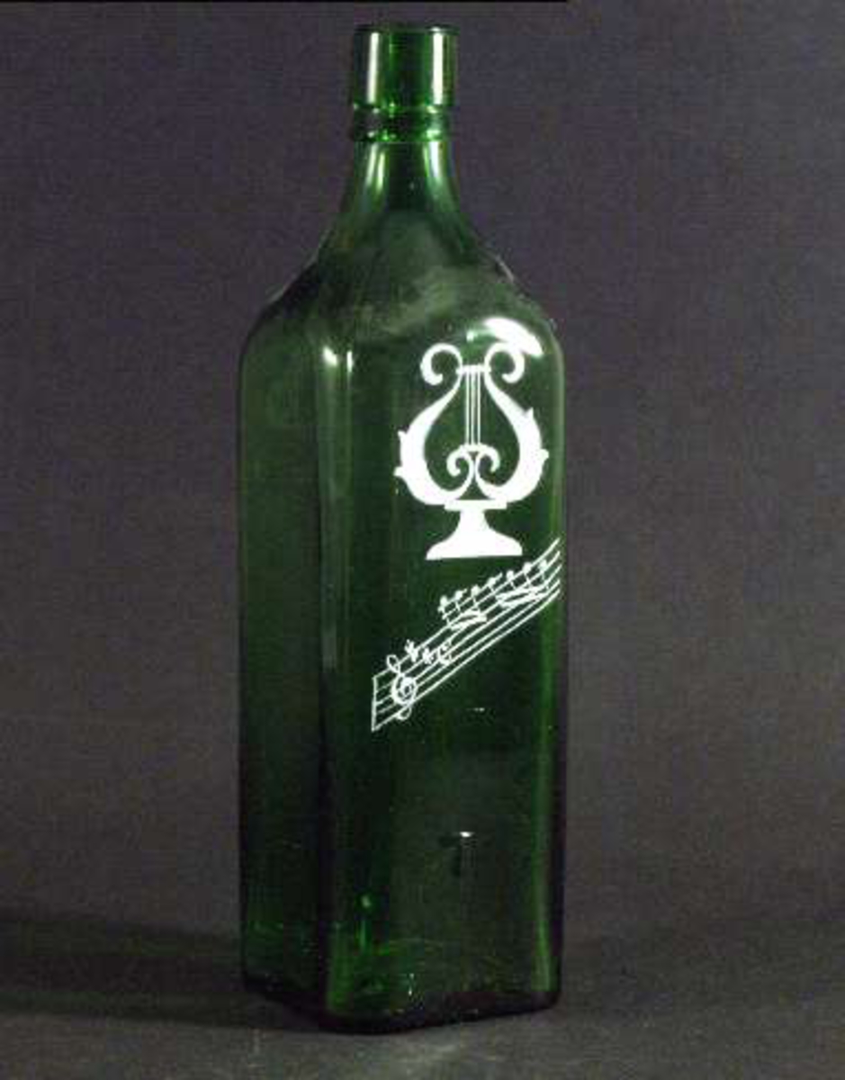 Flaska av grönt glas med T i relief och vitmålad dekor (lyra och noter). Märken efter formens skarvar.