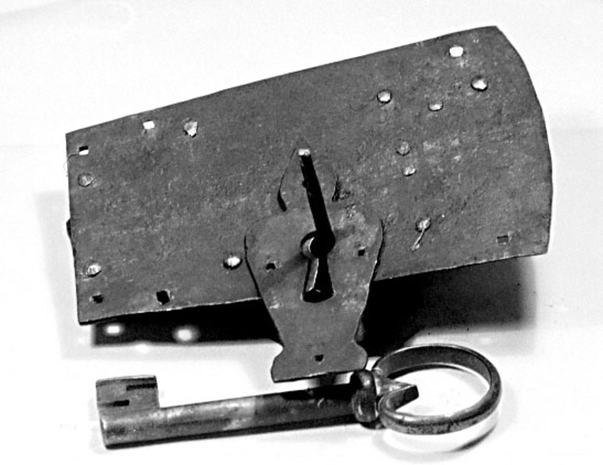 Fällbomslås med tillhörande nyckel och profilerat slutbleck, smitt av järn. Nyckeln är s.k. vridlåsnyckel med ögla (grepp).




