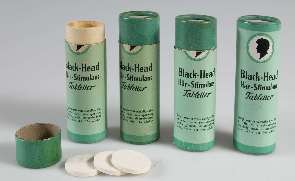 Fyra runda burkar av papp, gröna med svart text: Black-Head Hår-Stimulans Tabletter.