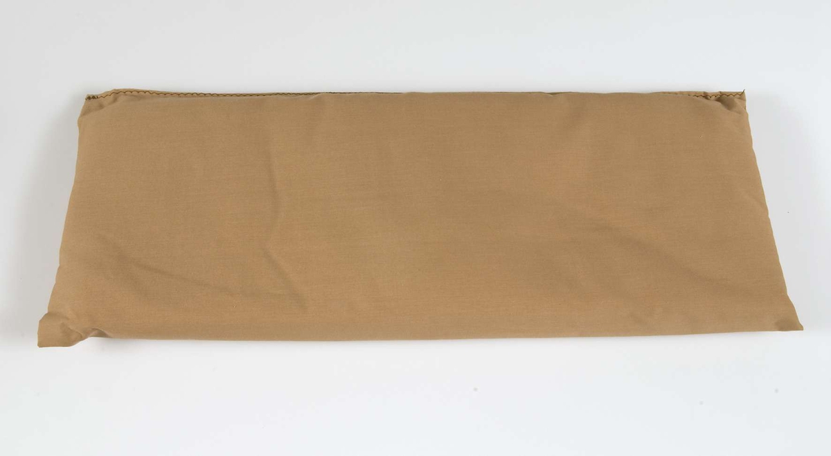 Madrass ingående i sängkläder till docksäng (vagga UM40571). Rektangulär madrass av brunt tyg, stoppad. Till sängkläderna hör också täcke, kudde och underlakan (UM40573a-c). Möjligen är madrassen tillverkad på senare tid.
