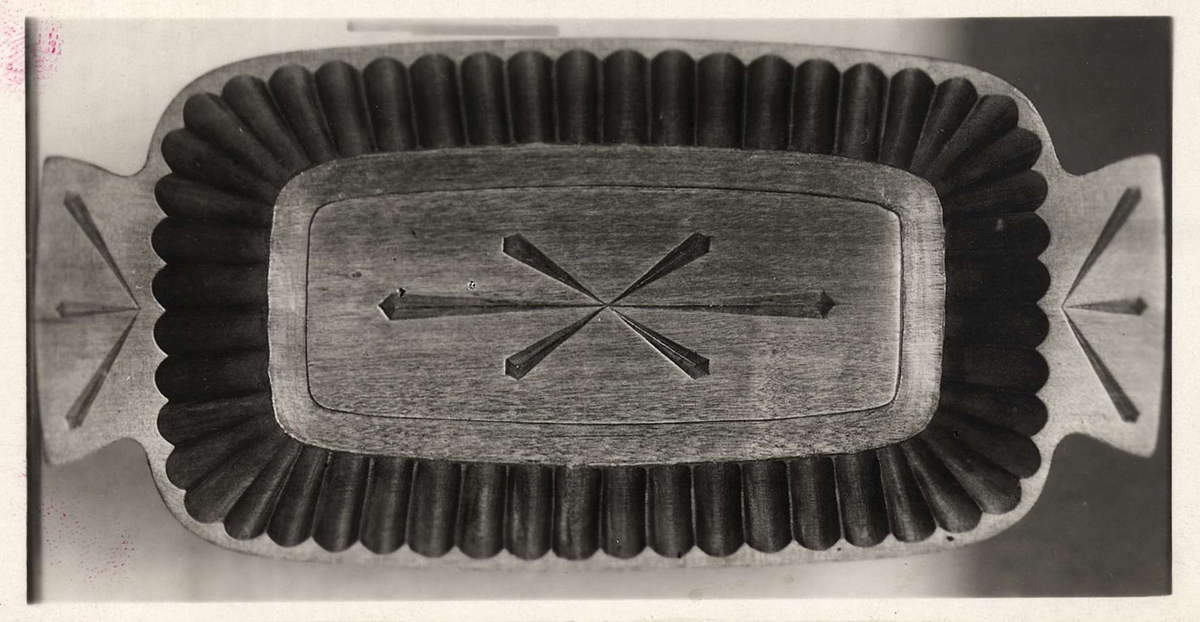 Ett grått 22 x 28 cm stort grått kartongblad med två fastklistrade svartvita fotografier. Fotografierna visar snidade träskålar. Vid ena fotografiet står "B-873" och vid andra fotografiet står "B-874".