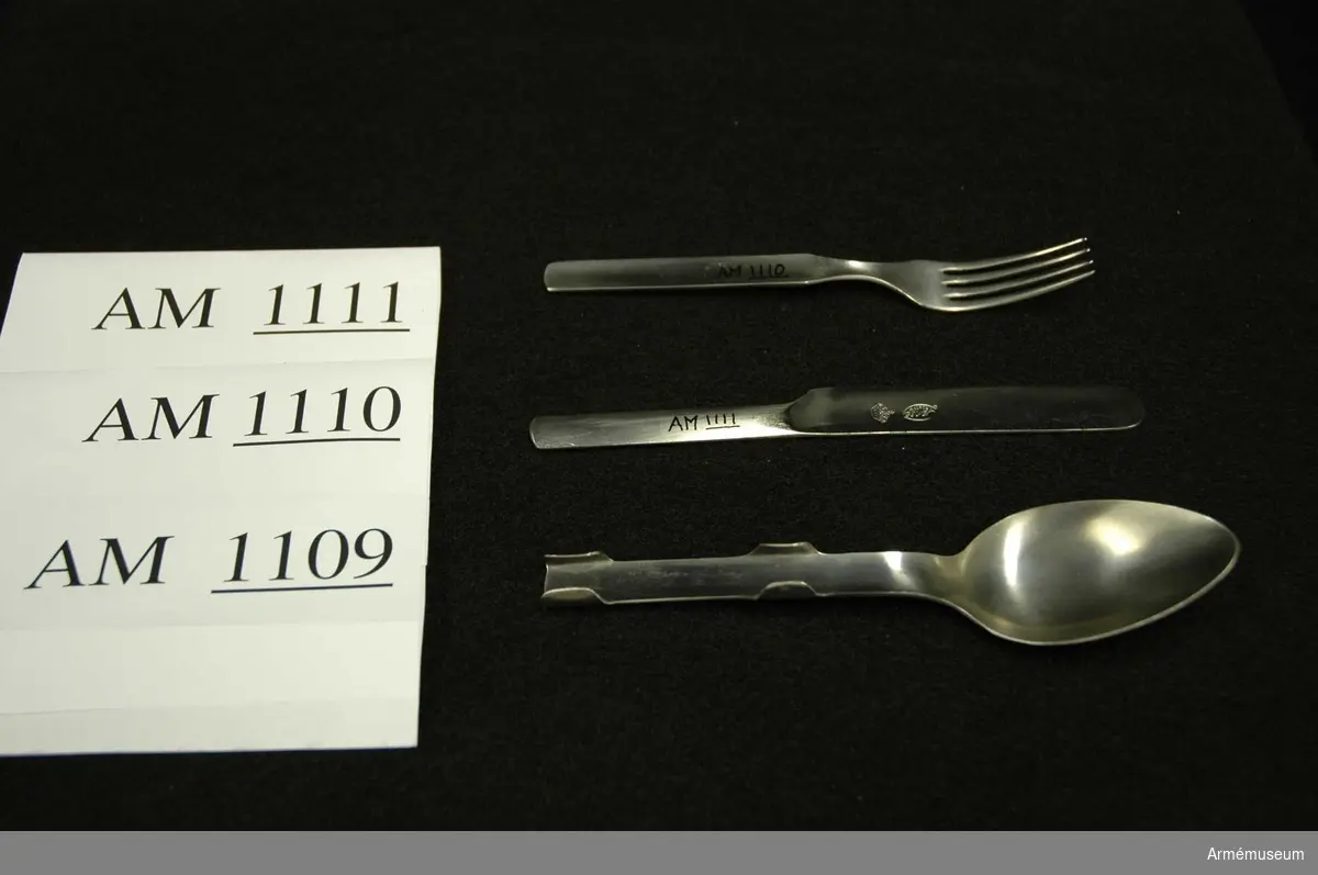 Samhörande nr är 1074-1129, (1109-1111).
Sked m/1929.
Utförd i ett stycke. Skaftet är försett med fyra falsar vilka håller sked, gaffel, och kniv förenade under förvaring och transport. Något speciellt märke för GENSE finns ej på skeden, endast kniven. Har tillhört mob.utrustning vid Armémuseum.