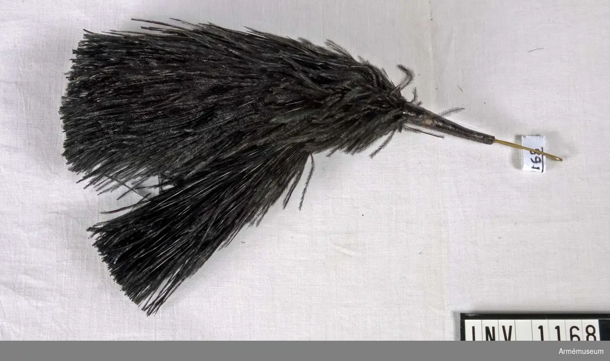 De svarta fjädrarna utgår från ett ställe där alla sitter fastgjorda i den böjda ståltråd som stoppas ned i pompongen. 110 mm är synligt vid användningen.