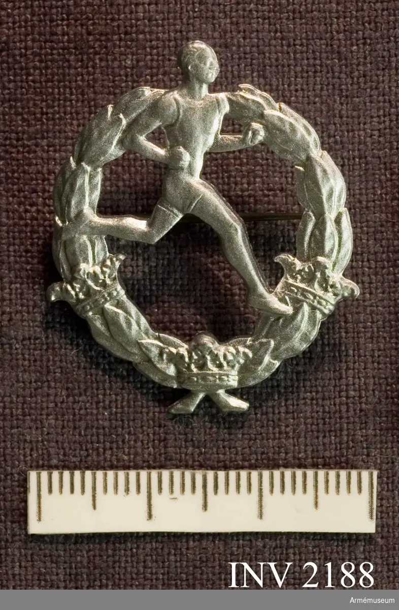 Samhörande nr är 2170-2188.Märke, friidrotts-, silver, generalitet.Lagerkrans med tre kronor och en löpande man. På baksidan "12299 Westins  Stockholm".