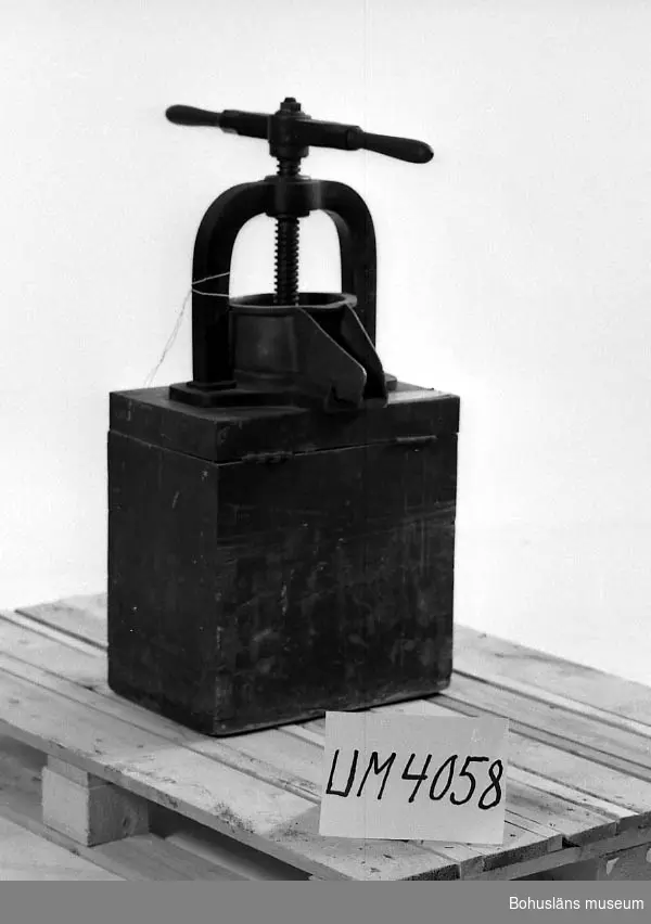Ur handskrivna katalogen 1957-1958:
Skålpress f. bl. a. tinkturkryddor.
H. (nedskruvad) 80 cm; en kraftig sockel av trä, som en låda, på vars "lock" pressen är fäst; en skål av mässing m. pip; en kraftig arm, L. 34,5 cm, att vrida; i en bygel av järn; "locket" är på gångjärn och genom att lyfta detta rinner det presssade ut. Järnet rostigt. Ett gångjärn trasigt.

Lappkatalog: 94