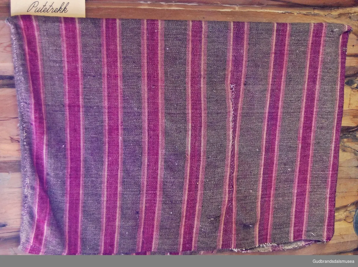 Vevd bolster, med striper i brunt, rosa og lilla.
