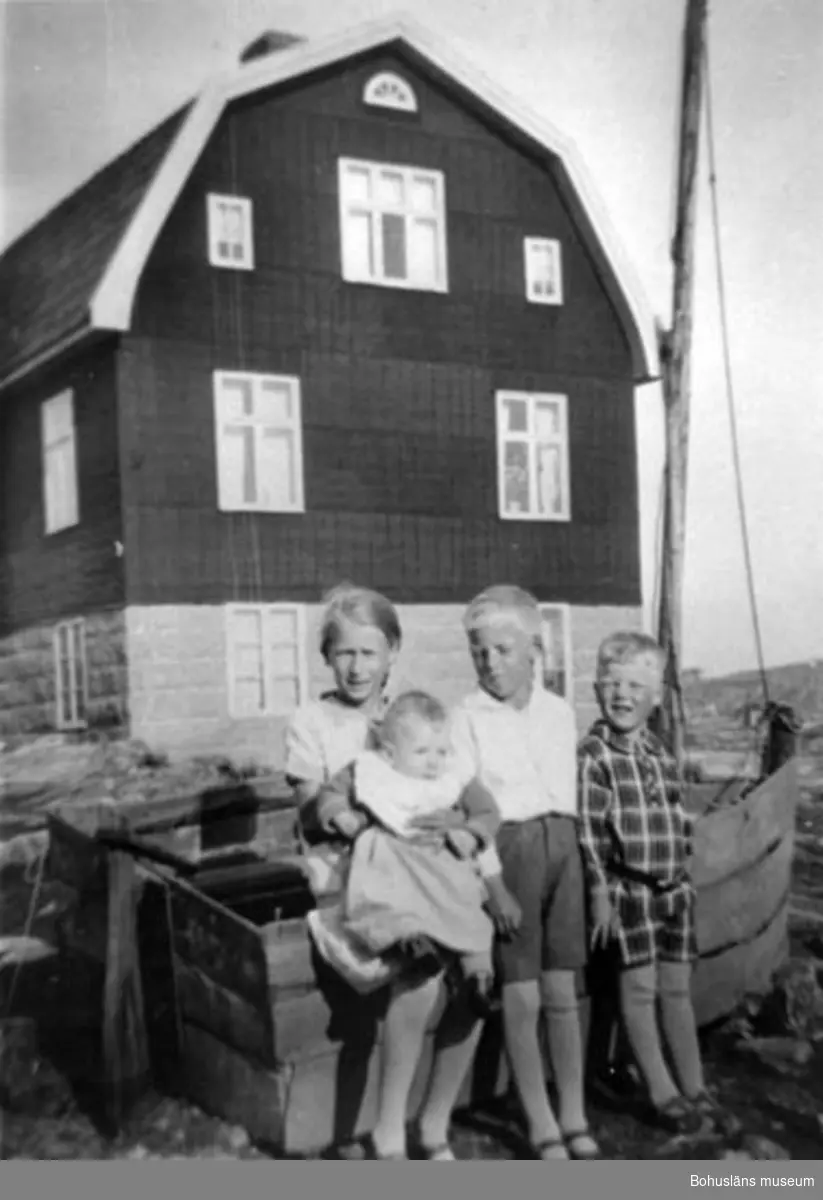 Enligt text på fotot: "Kalle på Sluttets hus och hans barn/Smögen Fr.v. Karin-Ingvar-Tore och lille Gunnar Karlsson taget omkring 1930, alltså 60 år 1990 OBS båten de står och lutar sig emot".