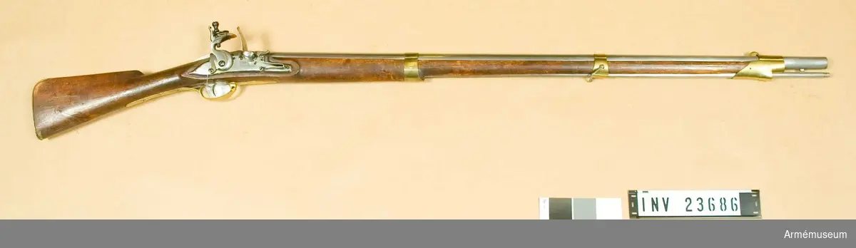 Samhörande nr är: 23686-7, gevär, bajonett.
Flintlåsgevär. Reparerad m/1805.
Grupp E II. 
Nominalkaliber 20,04 mm.  Verklig kaliber 19,85 mm.Geväret är sammansatt av delar från diverse äldre gevär.  Pipan är av 1725 års modell och filad rund.  Siktet är det ursprungliga, men med nedfilade vingar. Kornet är  av mässing, båtformigt och högt.  På pipans översida finns krönt N T (Norrtälje) T S och C G. På  vänstra sidan finns ett inslaget M och några otydliga stämplar.  På undersidan finns en otydlig stämpel och, täckt av laddstocks-  fjädern, en med bokstäverna P A. Häftena är bortfilade och pipan  är något förkortad. På pipans undersida, 4 cm bakom mynningen,  sitter en bajonettklack.Låset ser ut att vara m/1725. På bleckets utsida finns en stämpel med bokstaven B eller möjligen med ett monogram av I B.Stocken är mörkbrun, av björk och m/1805. På kolvens vänstra sida är bokstäverna T S och numret 35 inslagna.Sidblecket är taget från ett gevär m/1747. Det har på utsidan en stämpel med I P M och dessutom är där inslaget numret 179. På insidan sitter en stämpel med A S B. Övriga beslag är de vanliga m/1805. Bakplåten har en rätt lång, över kolvryggen utskjutande flik samt fasthålles genom en mindre skruv, som går genom denna flik, och genom två större, med stora stöthuvud försedda skruvar. På flikens översida sitter en otydlig kronstämpel och på bakplåtens insida finns bokstaven G. På varbygelns insida sitter en stämpel med S V. Nedre bandet har på undersidan en framåtriktad, avrundad spets. Mellanbandet är både fram och bak över laddstocksrännan litet utdraget. Näsbandet har kraftig, över laddstocksrännan gående kappa. Detta band och nedre bandet fasthålles av stift, mellanbandet av övre rembygelns skruv. Den nedre rembygelns skruv går genom varbygeln strax under dess främre ände.Laddstocken är cylindrisk. I ena änden har den gängor för kratsen. I samma ände är huvudet genombrutet av en 3 cm lång springa.I Modellsalens reversal återfinnes geväret som "Mousquetter och Infanteri Gevär. Svenska. Med flintlås. 1805 års reparationsmodell" och bajonetten under, "Bajonetter Infanterigevärs, Svenska, 1805 års reparationsmodell". Jfr AM 1932:4190