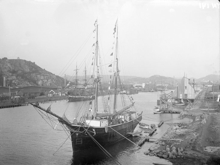 Tvåmastad slätskonare, troligen Ägil ex Sleipner, regnr 3035, med stor flaggning, i Uddevalla hamn. Briggen Emil i bakgrunden."