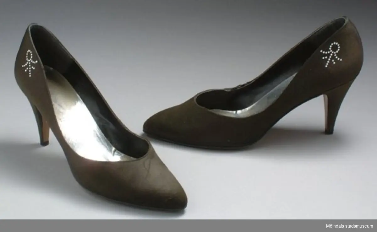 Brun/grå sko med hög klack. Bak på sidan sitter en liten silver utsmyckning.Måtten:Stl. 39, längd 270 mm, bredd 80 mm, höjd 150 mm (med klack).  