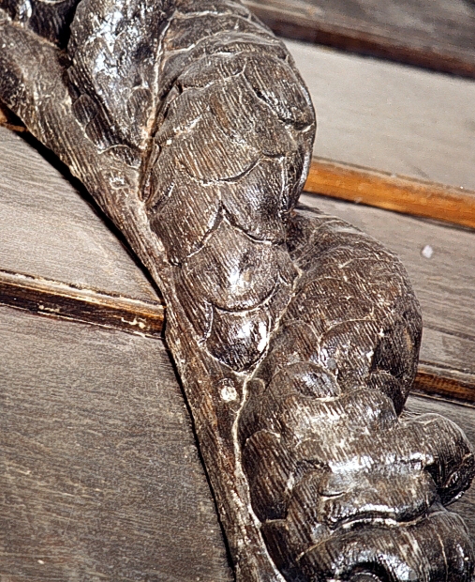Nereid med huvudet täckt av ett dok eller dylikt. Kring midjan sitter ett ovalprytt band. Bandet tycks vara hårt åtdraget och ger figuren därigenom kvinnliga former. Armarna är reducerade till upprullade bladflikar. Skulpturens fiskstjärt slingrar sig kring stjärten till en fisk eller en delfin vars huvud är synligt vid skulpturens fotända.

Bakstycket är kraftigt och snidat i ett med skulpturen. Baksidan är försedd med hak eller urtag. Skulpturens profil är svagt S-formad.
Skulpturen är kraftigt sliten och anletsdragen i det närmaste utplånade.

Text in English: Nereid with head covered by a hood or veil. Round the waist there is a girdle or belt with an oval decoration. The arms are replaced by rolled-up leafy decoration. The lower part of her body consists of a fish tail that is entwined with the tail of a fish or dolphin whose head can be seen at the foot of the sculpture.

The backboard is robust and carved in one piece with the figure. The back side of the backboard is carved with hollowed out grooves. The profile is slightly S-shaped.
The sculpture is badly worn and the facial features virtually erased.