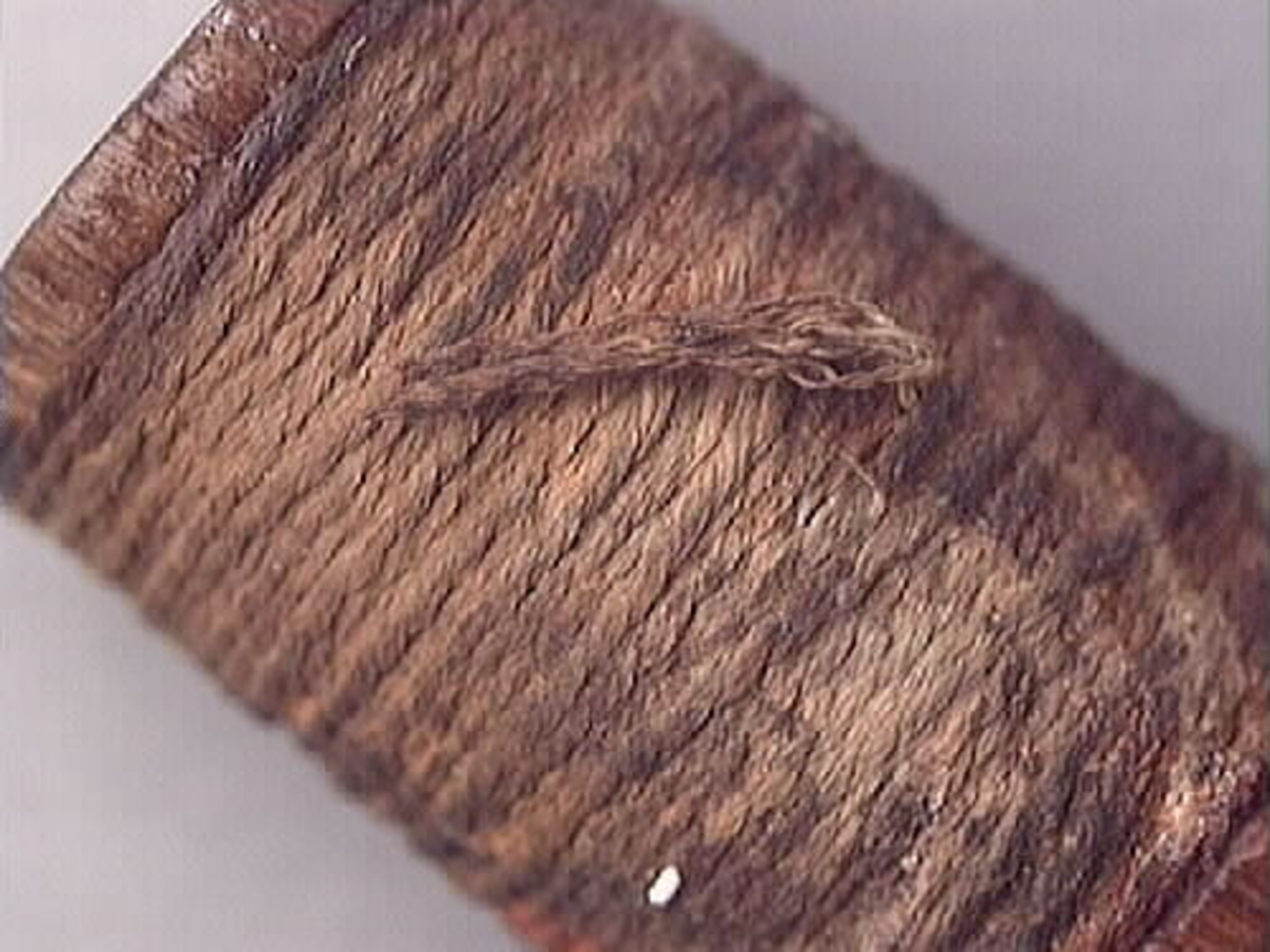 Trärulle med upplindad rev eller snöre. Rullen är rödaktig i färgen. Snöret har rostliknande fläckar. Trärullen och reven är välbevarad.