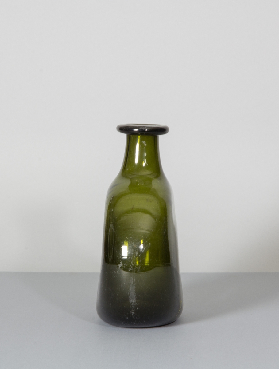 Flaska i grönt glas. Tillplattad modell med rundade sidor. Hals med bred halsring.
Likheter med den tyska Bocksbeutel.