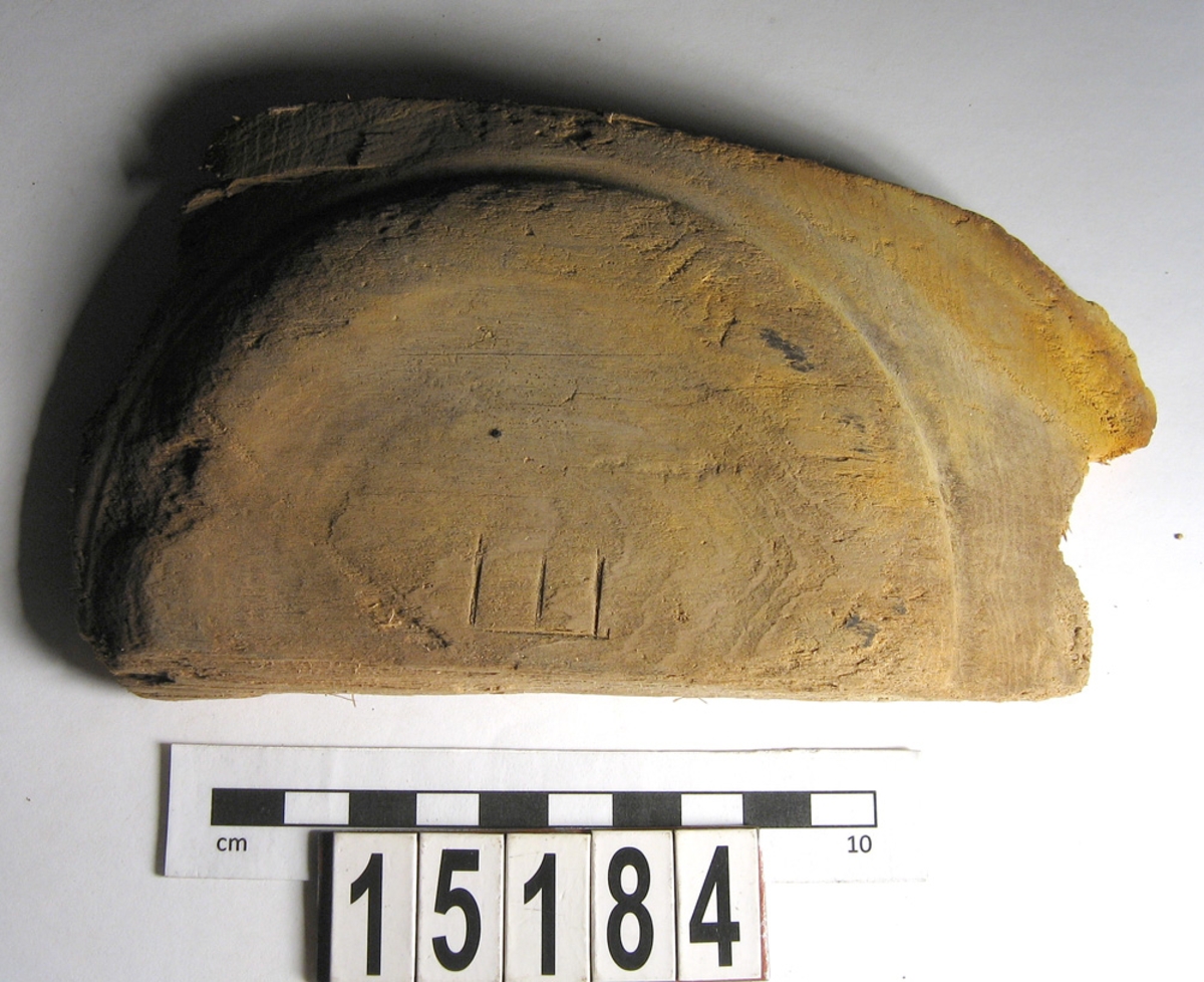 En del av en svarvad träskål. På baksidan syns ett inristat E.
Splittrad. Många skärmärken finns på skålens insida.