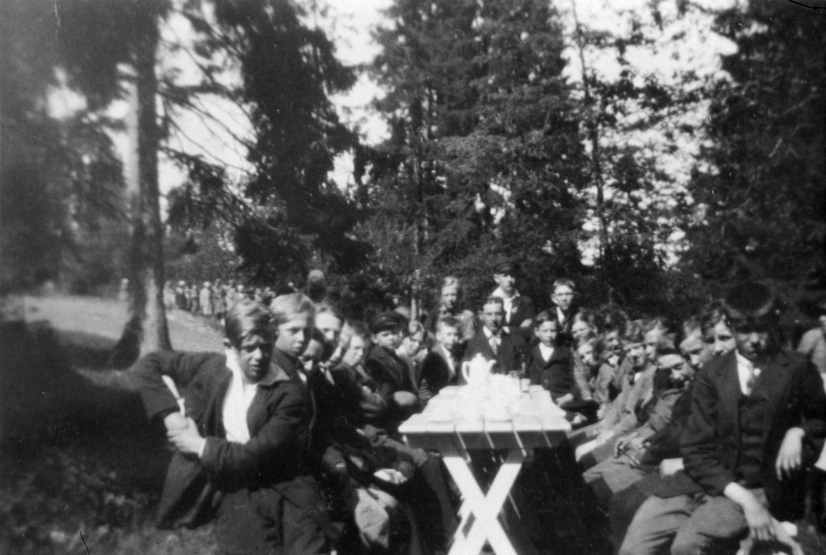 Pojkar sittande kring kaffebord i en park. Skolresa till Trollhättan. Åkte dit i likbil. Magister Villard Nilsson-Stockelids klass från Grevedämmets skola i Mölndal.