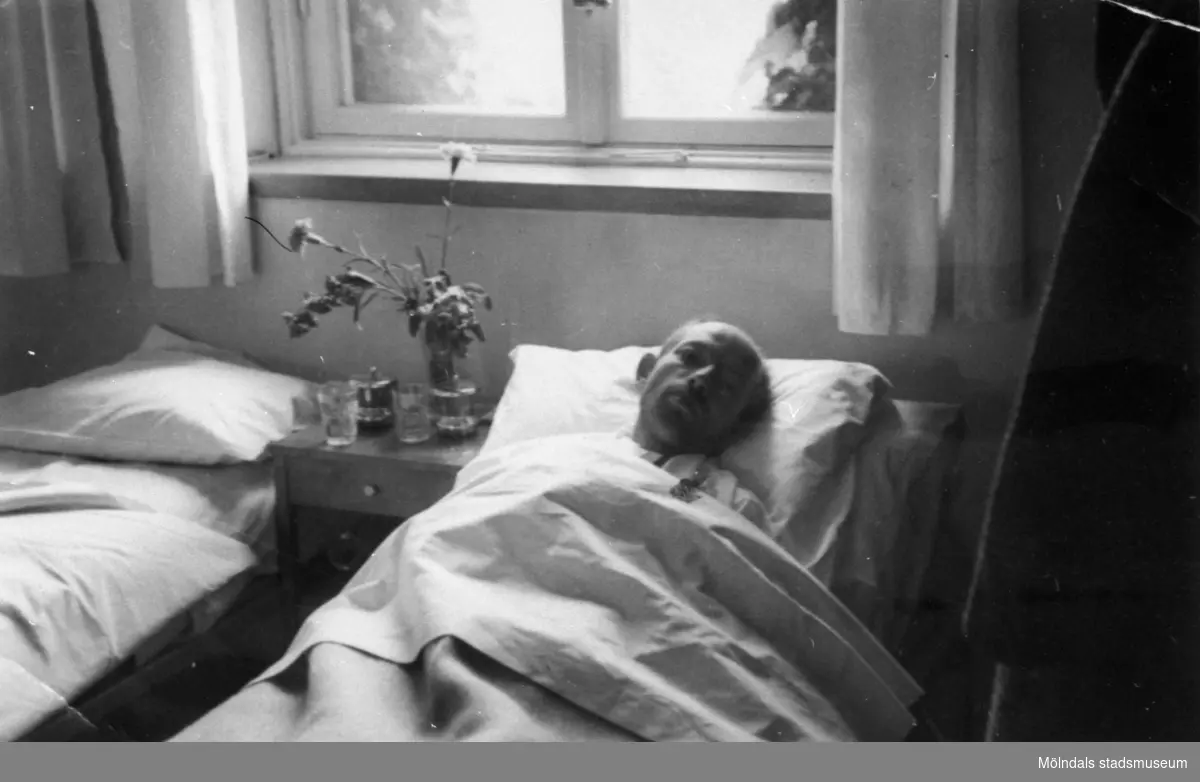 "Karantänsförläggning" på Kvarnbyskolan för överlevande från koncentrationsläger i Tyskland och Polen 1945.  
Skolan fungerade under denna sommar som beredsskapssjukhus.

En patient ligger i en säng i en sjuksal. På sängbordet till höger om mannen (till vänter i bild) står ett n vas med blommor.