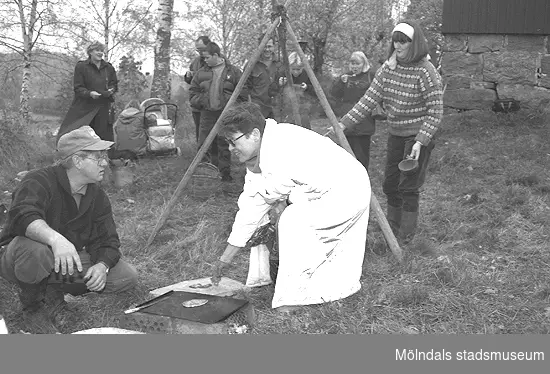 Familjesöndag vid Börjesgården, 1994-05-15. Museitekniker Alf Garthman sitter på huk och grillar. Museichef Mari-Louise Olsson kokar mat över öppen eld.