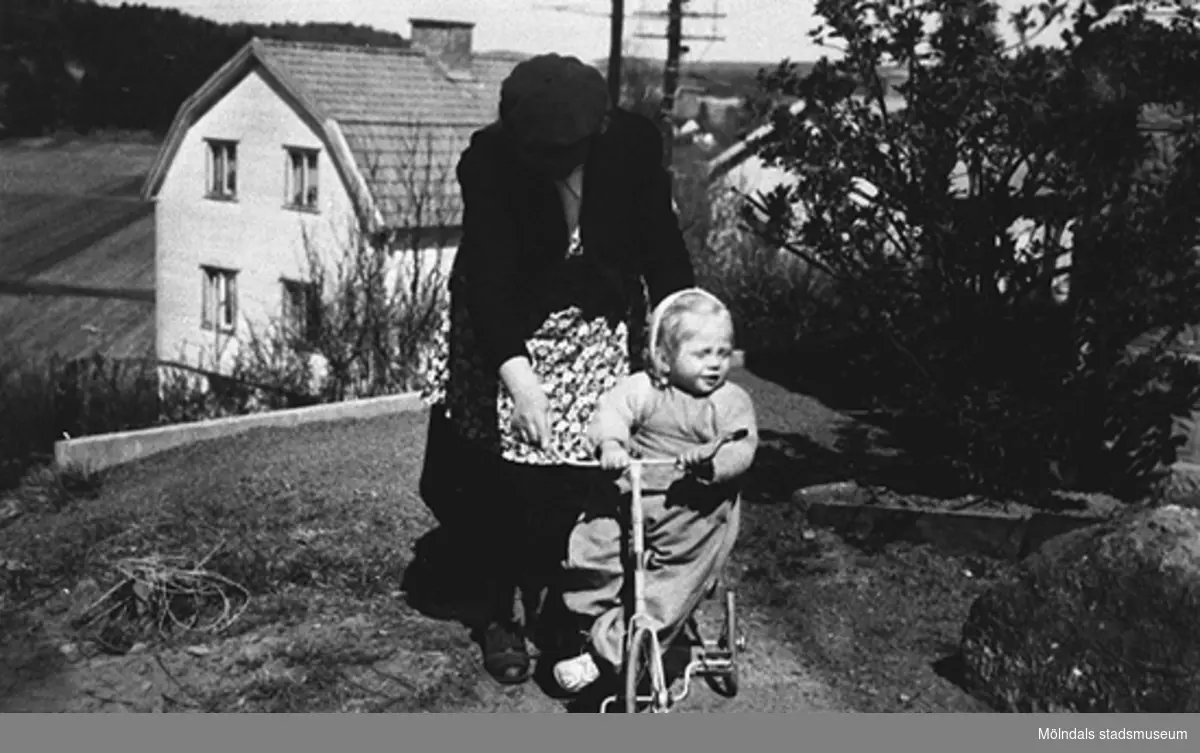 Mormor Nora Krantz hjälper Karin Pettersson (gift Hansson) att cykla på sin nya trehjuling, Gamlehagsvägen 17 i Torrekulla 1948.