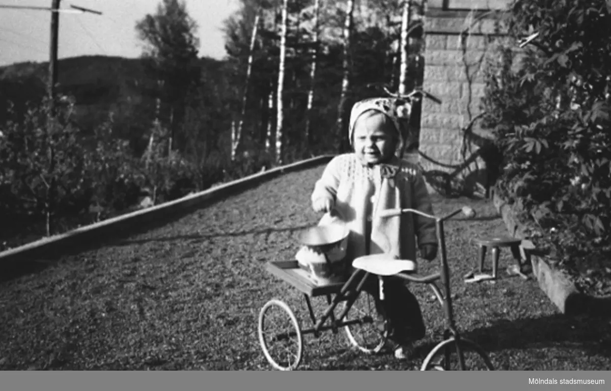Karin Pettersson (gift Hansson) står med sin trehjuling på grusgången utanför huset, Gamlehagsvägen i Torrekulla år 1948.