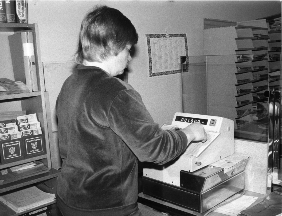 Postkassör Gerd Wikman slår in insatserna för strycktipset på den speciella kassaapparaten på postkontoret i Arvidsjaur. Ca 1983.