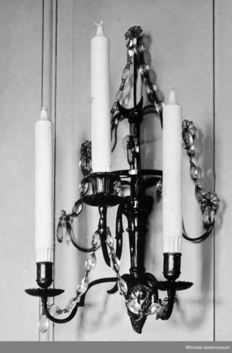 Vägglampett av metall med slipade kristallprismor samt hållare för tre ljus. Gunnebo slott, 1930-tal.
