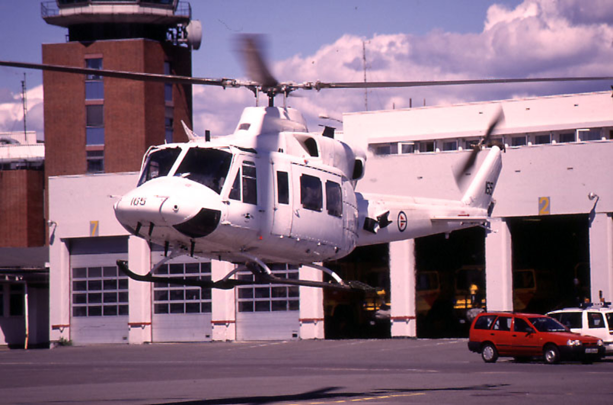 Lufthavn, 1 helikopter i ferd med å lande på rullebanen, Bell 412, 165 fra 720 skvadronen RNoAF.  2 kjøretøyer, 1 garasjebygning og kontrolltårnet i bakgrunnen.