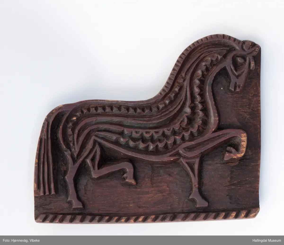 Motiv av en hest som løfter venstre bakfot og høyre framfot. Håndtak på baksiden.
