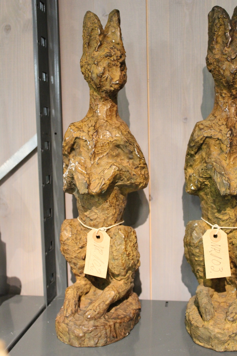 En skulptur i bronse av en hare sittende på to. Se også nr. 103 og nr. 104.