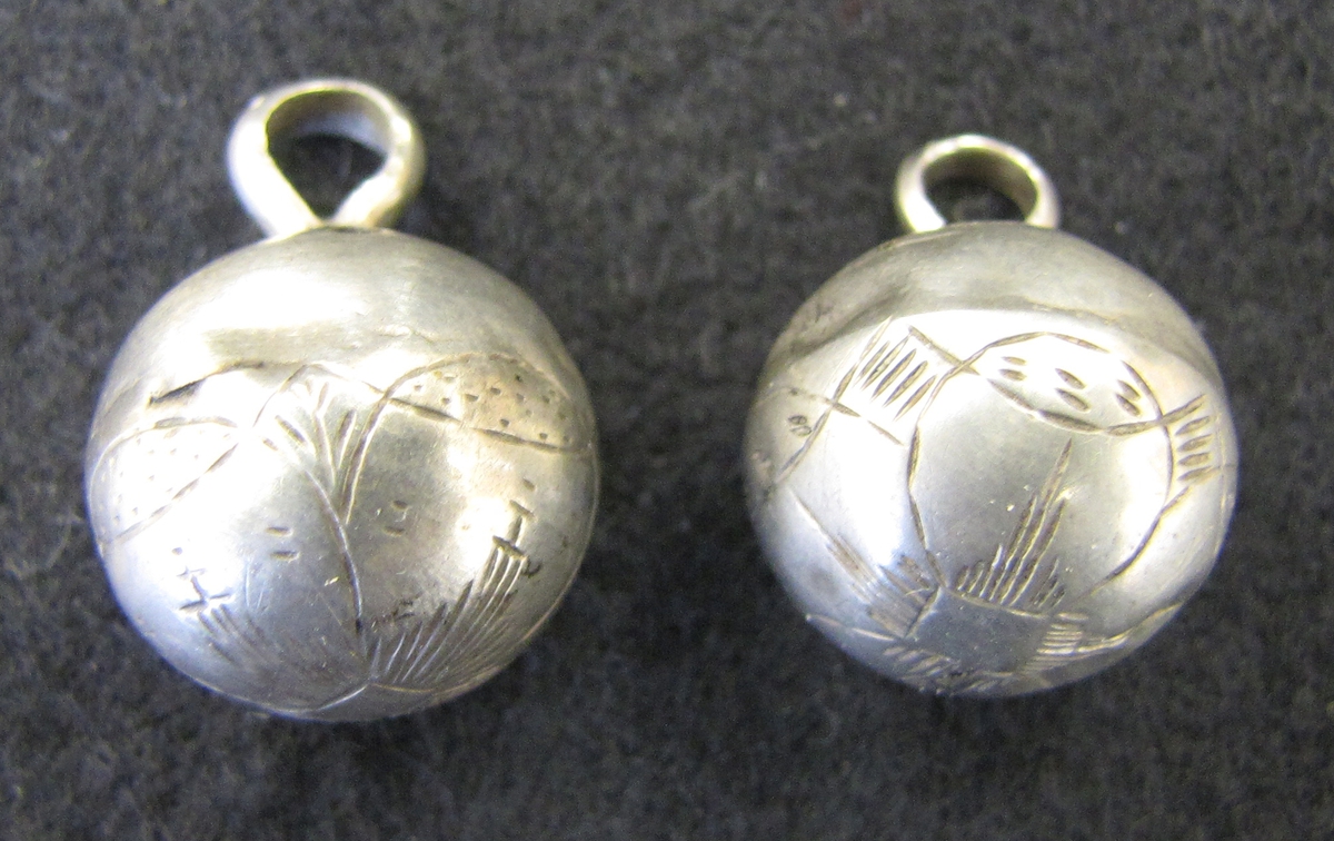 Två klotrunda, ihåliga, silverknapar, med en enkel, sliten, ingraverad blomdekor. Båda knapparna har mindre bucklor.

Stämpeln ''IA'' är osäker att hänföra till någon bestämd silversmed. Det finns emellertid stora likheter med Ystadmästaren Jonas Aspelin d.y:s stämpel. Aspelin var född i Ystad 1771 som son till silversmeden Jonas Aspelin d.ä. (1730-1802). Aspelin d.y. gick i lära hos sin far och blev gesäll 1790 och mästare 1796. Han stämplade i Ystad fram till 1827. Även Jonas Aspelin d.y.:s son, Jonas Aspelin den yngste (1806-1878), var silversmed i Ystd och stämpade ''IA'' åren 1831-1878.