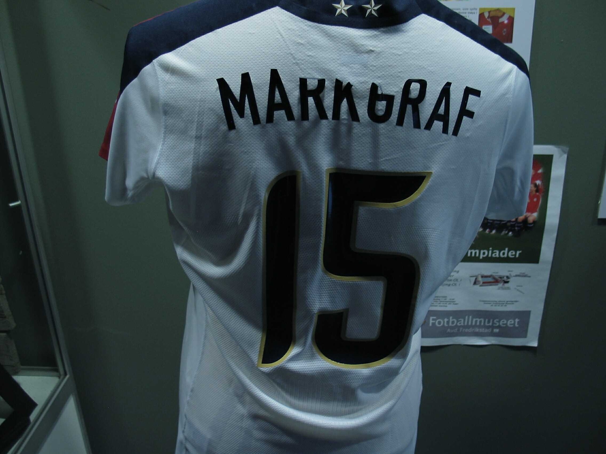 Hvit fotballtrøye. "Markgraff" i slitte bokstaver på ryggen. Signert av spillerne på det amerikanske kvinnelandslaget i fotball til OL i Beiijing. Dette laget vant senere OL.