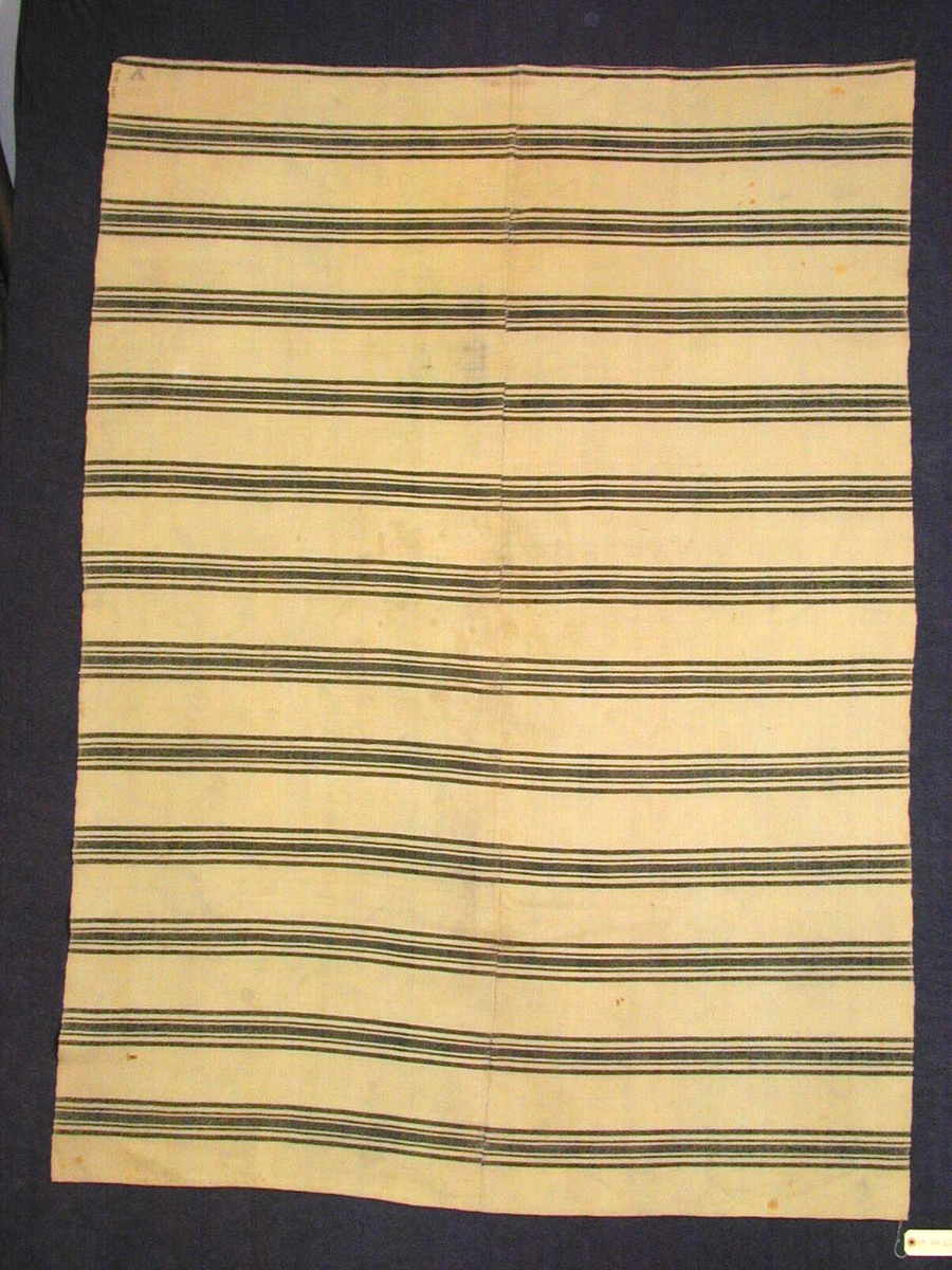 Mørke blå mønsterstripar i innslagsretning. 8,5 cm botnfarge mellom mønsterrapportane.Ein mønsterrapport her omlag 6 cm. brei og har 5 smale striper i ulik breidd : frå 0,3 cm til omlag 2 cm. med den breiaste stripa i midten.