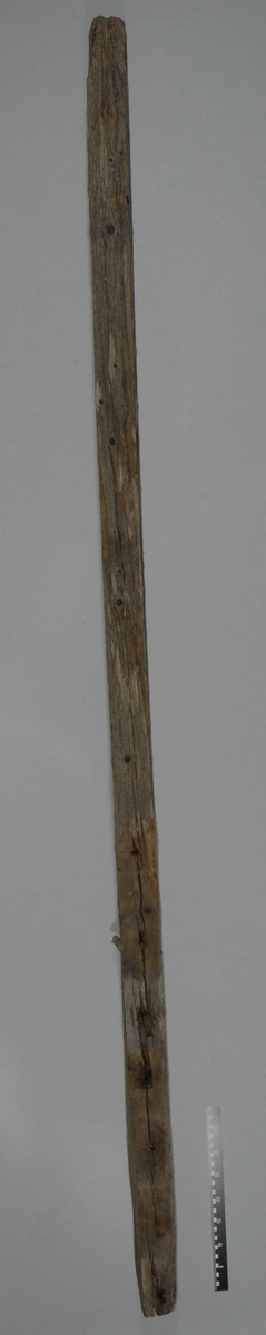Det er en lang firkantet trebjelke. Det er rester av tau som er festet som slynge i øvre delen av stolpen. Det kan være en bardunrest.Det er jernnagler i stolpen. Trematerialet er skjørt.