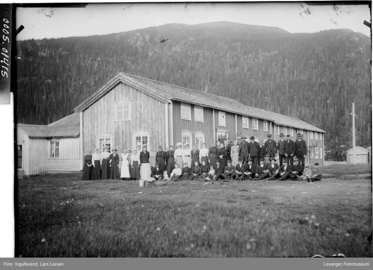 En forsamling av menn, kvinner og barn foran en bygning.