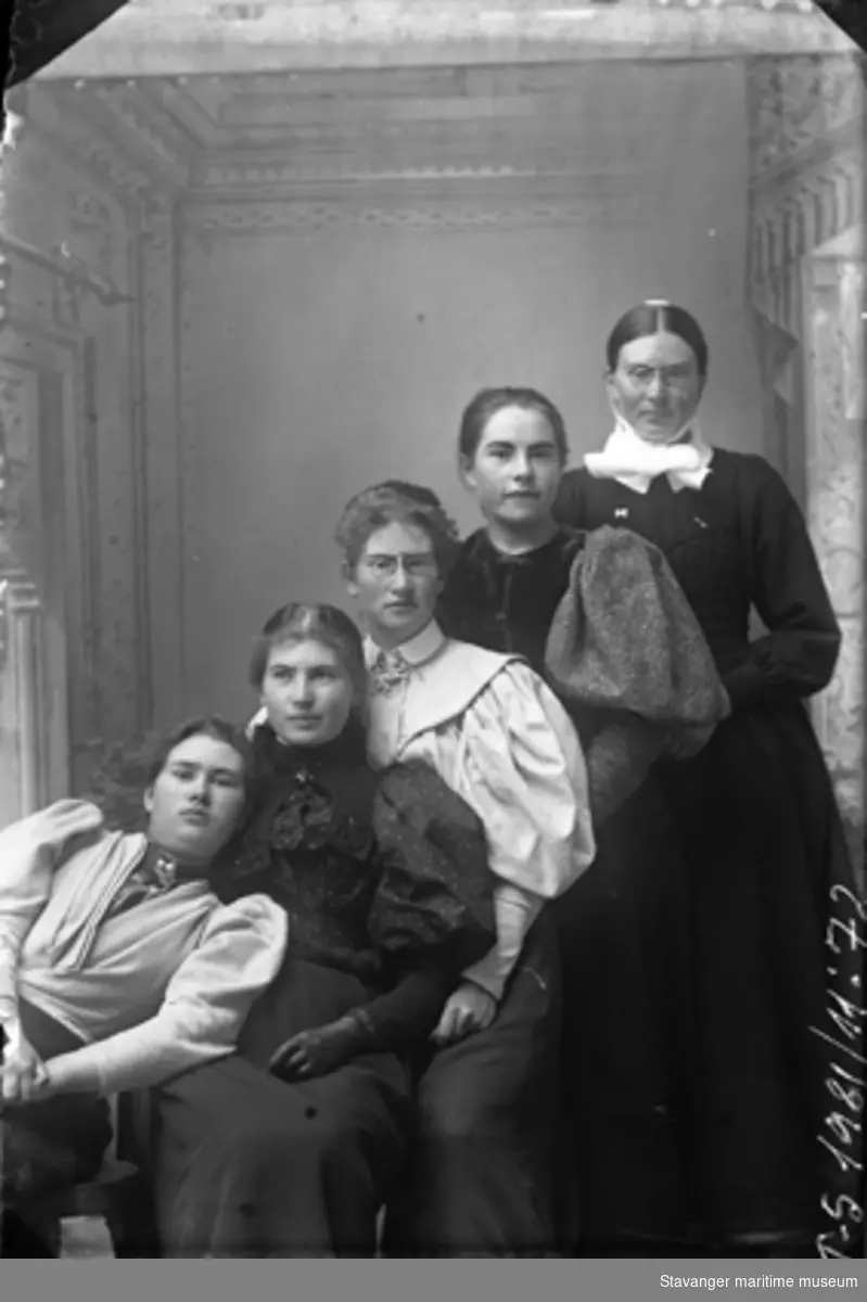 Atelierfoto av fem kvinner som står på rad. Den bakerste kvinnen er litt eldre og bærer sykepleieruniform. Kvinnen i midten har en brosje av "den norske løve" i halsen på blusen.